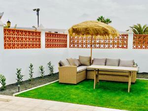 a patio with a couch and an umbrella and grass at Golden Wave Surf Villa in Corralejo