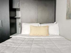Una cama con sábanas blancas y una almohada amarilla. en Sleepover Studio Apartments Downtown Springfield, en Springfield