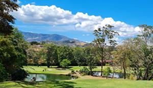 Ciudad Cariari的住宿－LOP Inn San Jose Aeropuerto - Costa Rica，一座带池塘和山脉的高尔夫球场