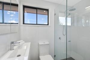 a white bathroom with a toilet and a glass shower at Lakeside Tranquillity in The Entrance