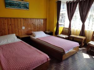 two beds in a room with two chairs and windows at Hotel Mhelung in Darjeeling