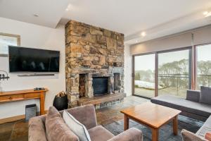 a living room with a stone fireplace and a tv at Alpine Woodsmoke Apartments in Falls Creek