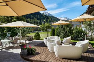 un patio con sillas blancas, mesas y sombrillas en Brugger's Genießerhotel Lanersbacherhof, en Tux
