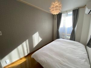 1 dormitorio con cama blanca y ventana en Villa Monica en Nagoya