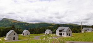 um grupo de casas numa colina com montanhas ao fundo em Les Burons du Mont-Dore em Le Mont-Dore