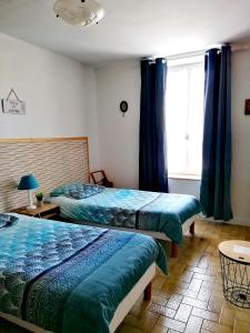 two beds in a bedroom with blue curtains and a window at La maison du Perrin in Gréez-sur-Roc