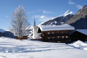 een kerk in de sneeuw voor een berg bij Gasthaus Oberweissen-Hittl in Sankt Jakob in Defereggen