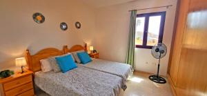 a bedroom with a bed with blue pillows and a fan at Holiday flat BLUE OCEAN, beachfront, sea view, 1 bedroom, livingroom, fast internet in Costa Calma