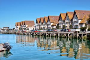 a river with houses and a dock with a boat in the water at Sénane - Joli studio à 50m de la plage, parking in Courseulles-sur-Mer