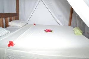Una cama blanca con dos flores rojas. en Union Beach Bungalow en Nungwi