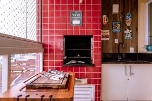 a kitchen with a red tiled wall with an oven at VARANDA GOURMET c churrasqueira-3 quartos- Wi-fi in Bertioga