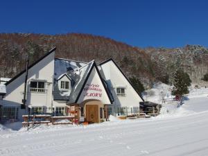 a large white building in the snow with a mountain at Pension Kaoru in Kiso