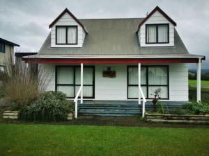 a white house with a porch and a lawn at Hosts on the Coast Dad's Place in Whangamata