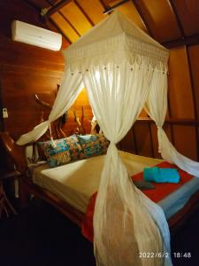 a bedroom with a canopy bed with white curtains at Kampung Meno Bungalows in Gili Meno
