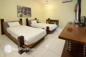 - une chambre avec 2 lits, une table et un bureau dans l'établissement Rumah Palagan Yogyakarta RedPartner, à Ngaglik