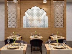 uma sala de jantar com mesas e cadeiras e uma parede em Novotel Makkah Thakher City em Meca