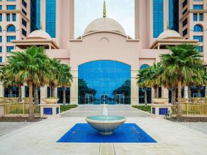 a fountain in front of a building with palm trees at Rixos Marina Abu Dhabi in Abu Dhabi