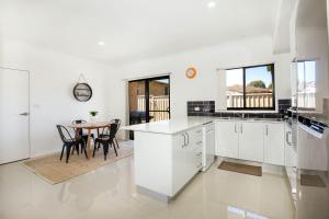 eine Küche mit weißen Schränken und einem Tisch mit Stühlen in der Unterkunft Villa Mare I 4 Mins to Beach in Culburra Beach