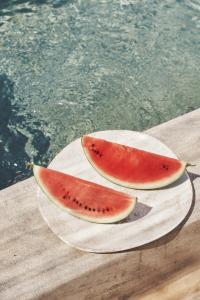 zwei Stücke Wassermelone auf einer Papierplatte neben einem Pool in der Unterkunft Under the Sun Cycladic Village in Tinos