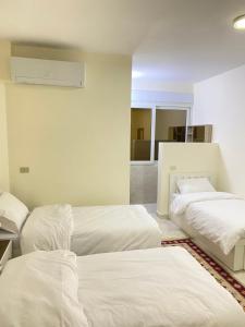 two beds in a room with white sheets at Rose city inn in Wadi Musa
