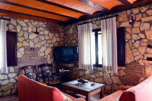 sala de estar con pared de piedra y TV en Casa Rural El Tejar Viejo, en Carcabuey