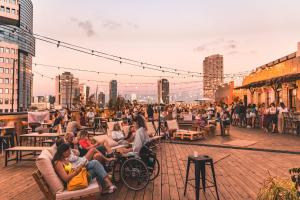 uma multidão de pessoas sentadas em um deck com um horizonte da cidade ao fundo em Selina Tel Aviv Beach em Tel Aviv