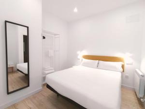 1 dormitorio con cama blanca y espejo en Apartamentos La Brava by gaiarooms, en Salamanca