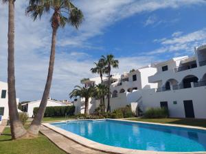 una piscina con palmeras frente a un edificio en Apartamento Son Parc Menorca, en Son Parc