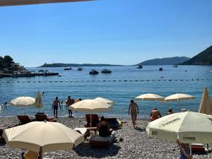 a group of people sitting on a beach with umbrellas at Apartments Marović in Luštica
