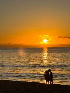 um homem e uma criança de pé na praia ao pôr do sol em Flower Garden Self-Catering Apartments em Beau Vallon