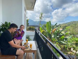 un hombre y una mujer sentados en un balcón comiendo comida en Santiago Bed and Breakfast at Desa Wisata Moni, en Kelimutu