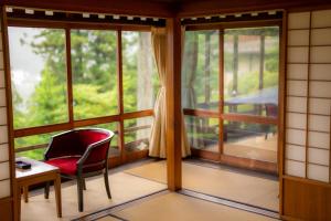 a room with a red chair and a table and windows at Yunoshimakan in Gero