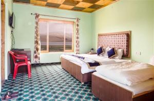 a bedroom with two beds and a red chair at Tsomoriri Hotel Lake View in Karzok Gömpa