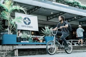 mężczyzna jeżdżący na rowerze przed sklepem w obiekcie AIEN Coffee & Hostel w mieście Chatan
