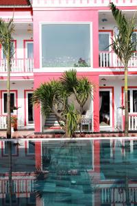 a pink building with palm trees and a swimming pool at Red House Homestay - Villa in Hoi An