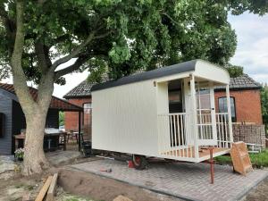 a white tiny house sitting next to a tree at Glamping De Vrije Wind, Tentverhuur in Houwerzijl