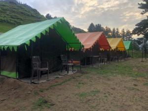 une rangée de tentes avec des chaises dans un champ dans l'établissement City Escape Camps and Cafe Kheerganga, à Kheerganga