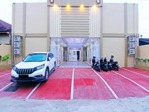 un coche blanco aparcado en un estacionamiento con motocicletas en OYO 90978 Khalifi Guesthouse Syariah, en Padang