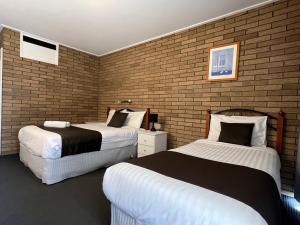 una camera con due letti e un muro di mattoni di Warrina Motor Inn Wodonga CBD a Wodonga