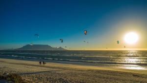 two people are flying kites on the beach at Sunset beach backpackers in Bloubergstrand