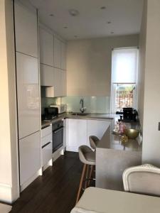 a kitchen with white cabinets and a table and chairs at Stylish 3-bedroom flat in Kensington in London