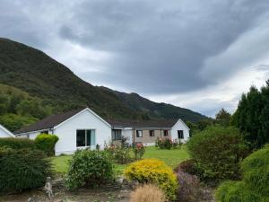 une maison blanche avec des montagnes en arrière-plan dans l'établissement Lyn leven cottages, à Ballachulish