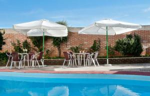Dois guarda-sóis brancos, mesas e cadeiras junto a uma piscina em Hospedium Hotel Juan II em Toro