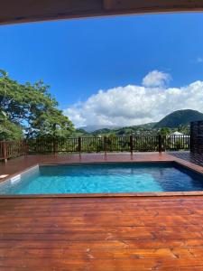 una piscina en una terraza de madera con montañas al fondo en Villa Auya entre mer et montagne en Le Carbet