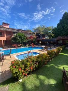 a resort swimming pool with tables and chairs and flowers at Pousada Saudosa Maloca in Arraial d'Ajuda