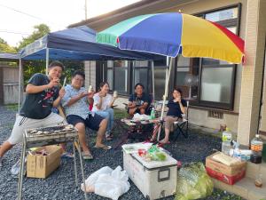 um grupo de pessoas sentadas sob um guarda-chuva em 島の宿　結んちゅ em Amami