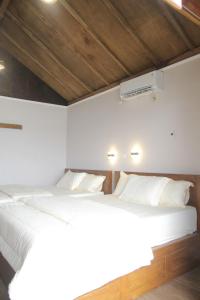 1 dormitorio con 2 camas blancas y techo de madera en Teras Pahawang, en Sukojayo