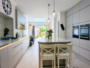 a kitchen with white cabinets and a kitchen island with two chairs at Beautiful 4 Bed Portsmouth Home Bright & Modern with Garden & Free Parking & Spa Bath & Fully Equiped Kitchen Perfect For Work or The Family in Portsmouth