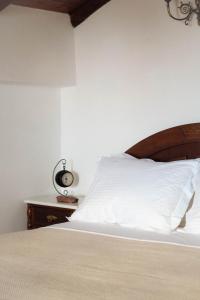 a bed with white sheets and a clock on a table at Castello di Haria in Kaloú