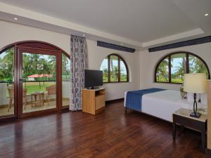 a bedroom with a bed and a tv and windows at Holiday Inn Resort Goa, an IHG Hotel in Cavelossim